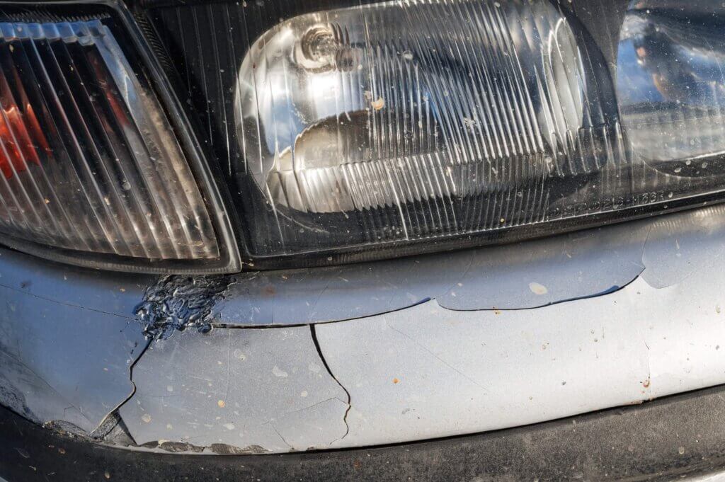 Ein Auto nach einem Unfall mit zerkratztem Scheinwerfer, gesprungener Stoßstange und abgeplatztem Lack – die Versicherung kommt nicht dafür auf