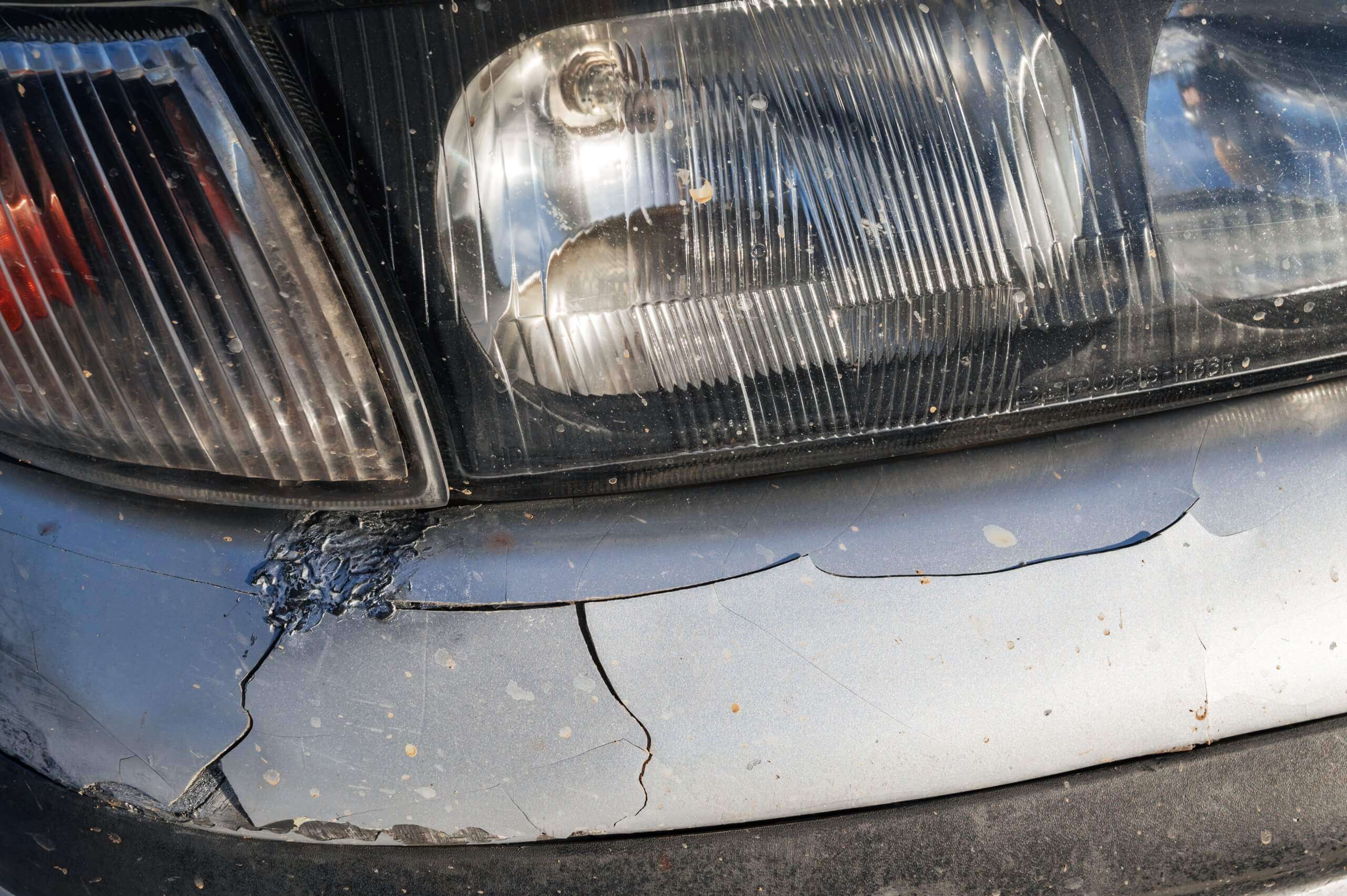 Ein Auto nach einem Unfall mit zerkratztem Scheinwerfer, gesprungener Stoßstange und abgeplatztem Lack – die Versicherung kommt nicht dafür auf