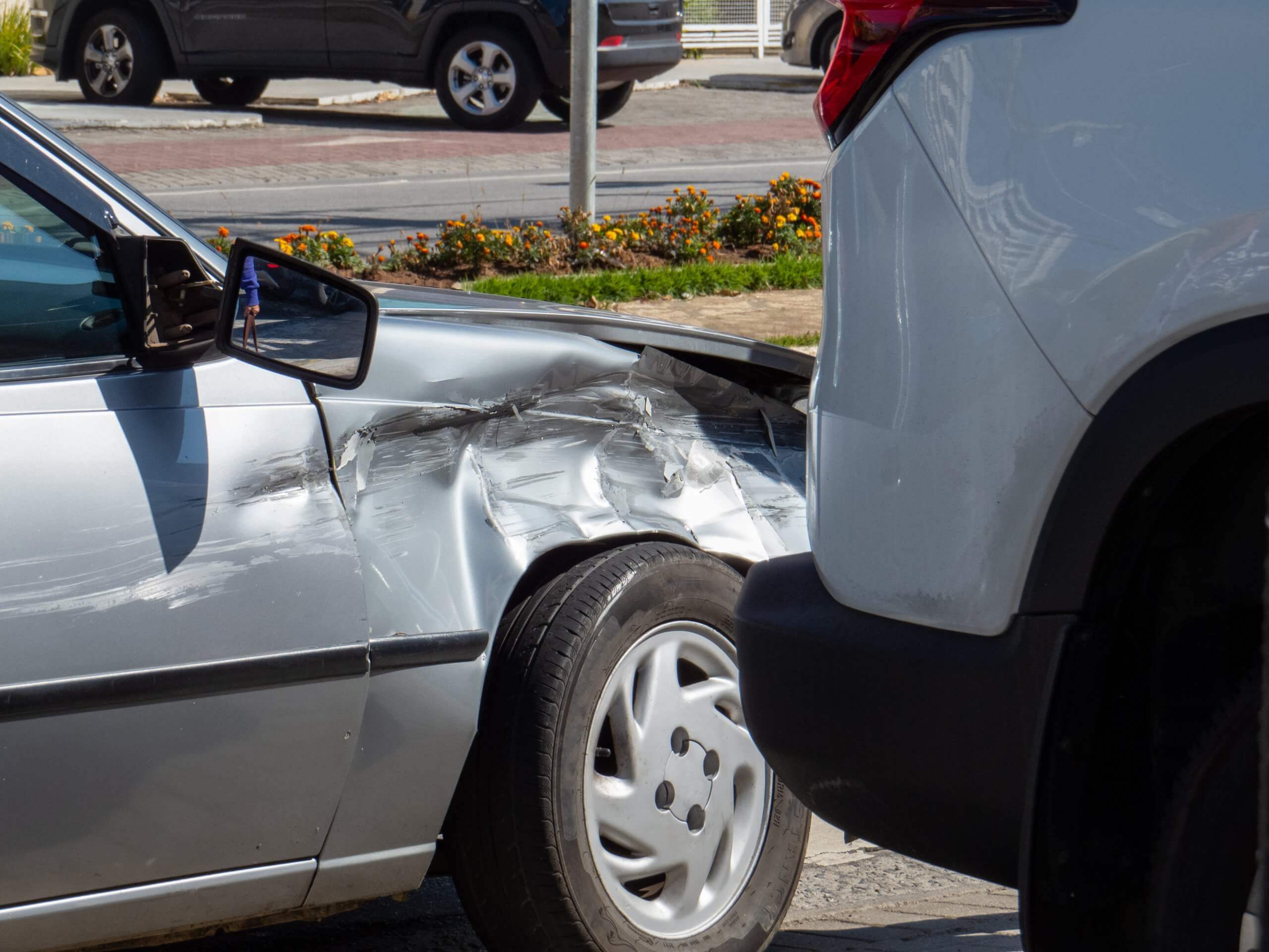 Ein silbernes Auto mit eingedrücktem Kotflügel nach einem Unfall mit einem weißen SUV; die Versicherung übernimmt keine Kosten für den Schaden